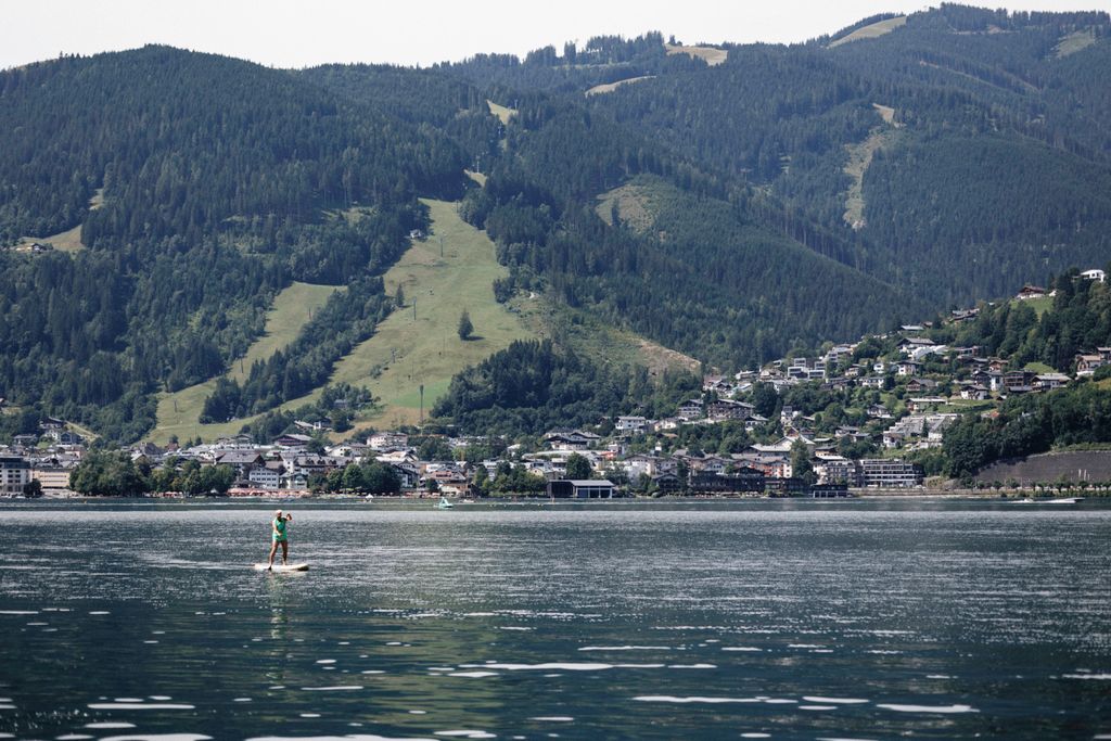 A person paddleboarding on Lake Zell, with scenic views of the Salzburg mountains and Zell am See town.