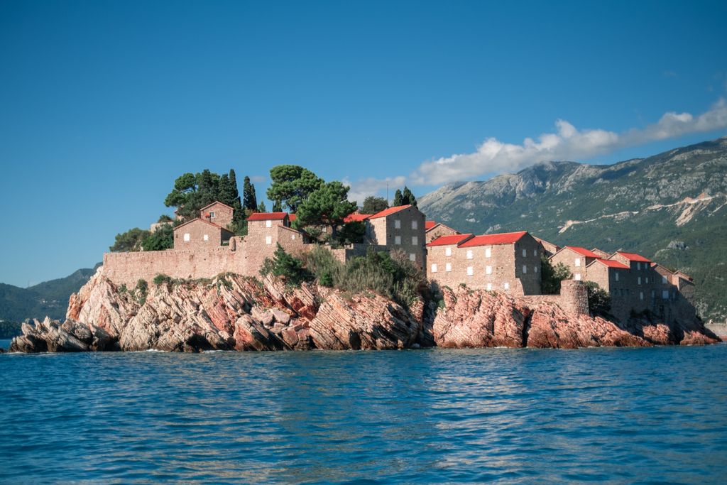 Sveti Stefan, Montenegro, stunning island fortress with red-roofed buildings on the Adriatic Sea, framed by mountains.