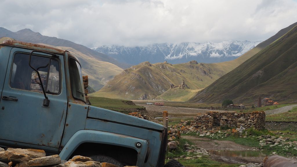 A vintage truck amidst the stunning landscapes of the Truso Valley, Georgia, showcasing snow-capped mountains and cultural heritage.