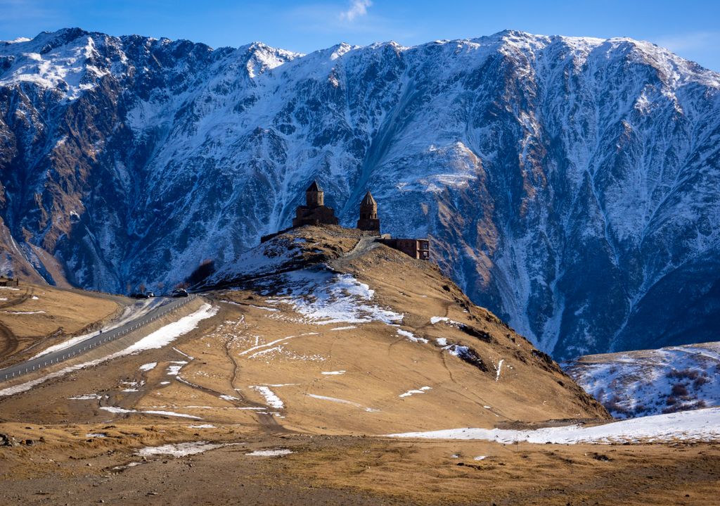 Scenic view of Gergeti Trinity Church against the backdrop of snow-covered Caucasus mountains in Georgia.
